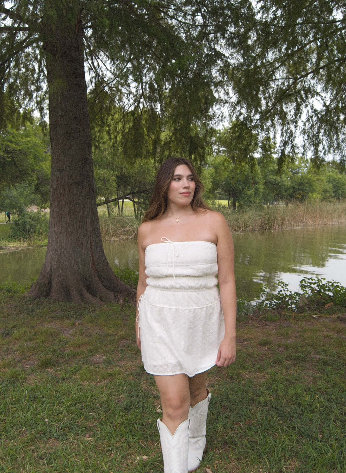 strapless white mini dress with eyelet pattern, tie sides, tie on the front. on model in front of lake.