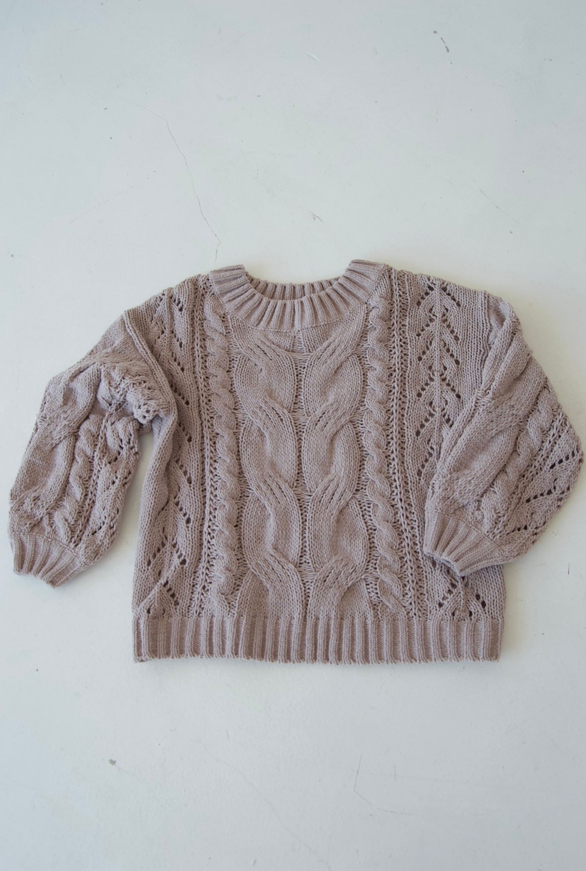 Picture features an off the shoulder neutral cable knit sweater on a flat lay.