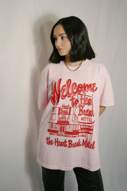 light pink graphic tee with heartbreak motel on it in bright red colors and graphics