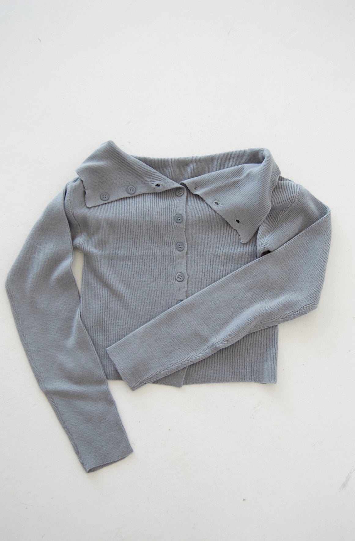 Picture features an off the shoulder blue cardigan with buttons on a flat lay.