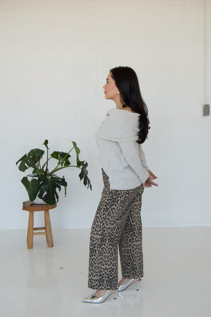 Picture features a light grey off the shoulder sweater on a model wearing cheetah print jeans and silver heels.