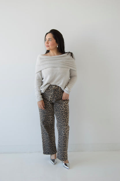 Picture features a light grey off the shoulder sweater on a model wearing cheetah print jeans and silver heels.