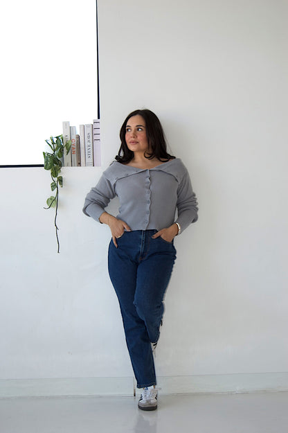 Picture features an off the shoulder blue cardigan with buttons on a model wearing blue jeans and Samba sneakers.