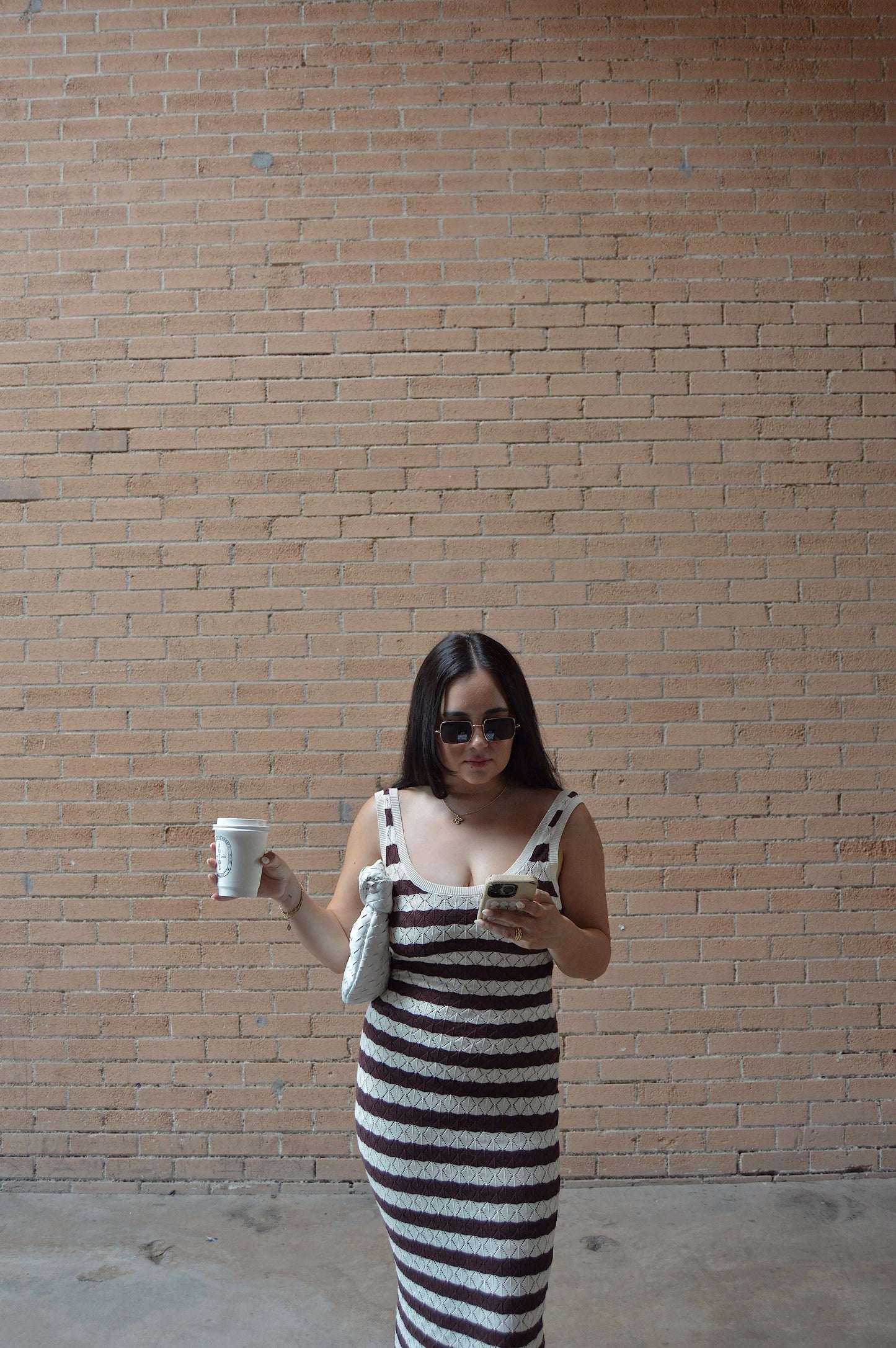 brown and white striped knit maxi dress on model posing with coffee and purse