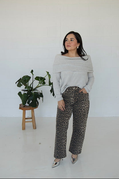 Picture features a light grey off the shoulder sweater on a model wearing cheetah print jeans and silver heels.