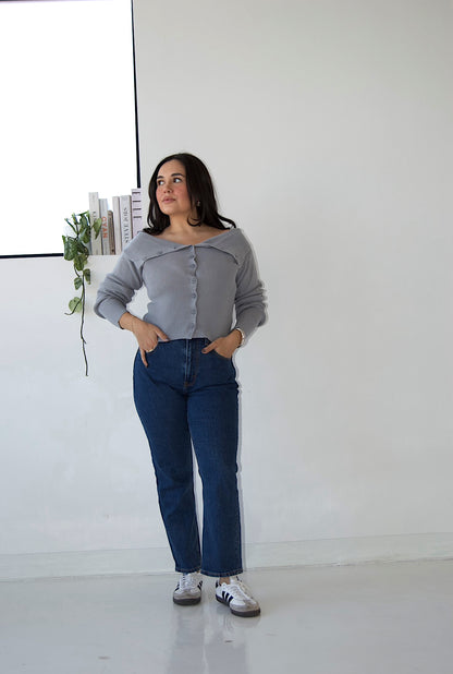 Picture features an off the shoulder blue cardigan with buttons on a model wearing blue jeans and Samba sneakers.